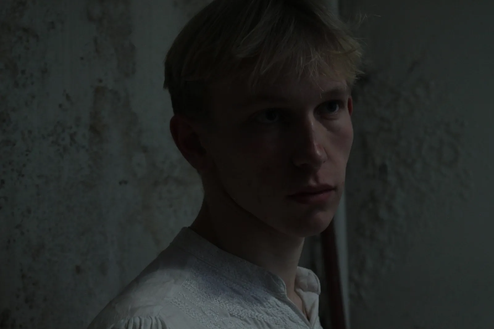 Promotional portrait of Orpheus against a bare plaster wall.