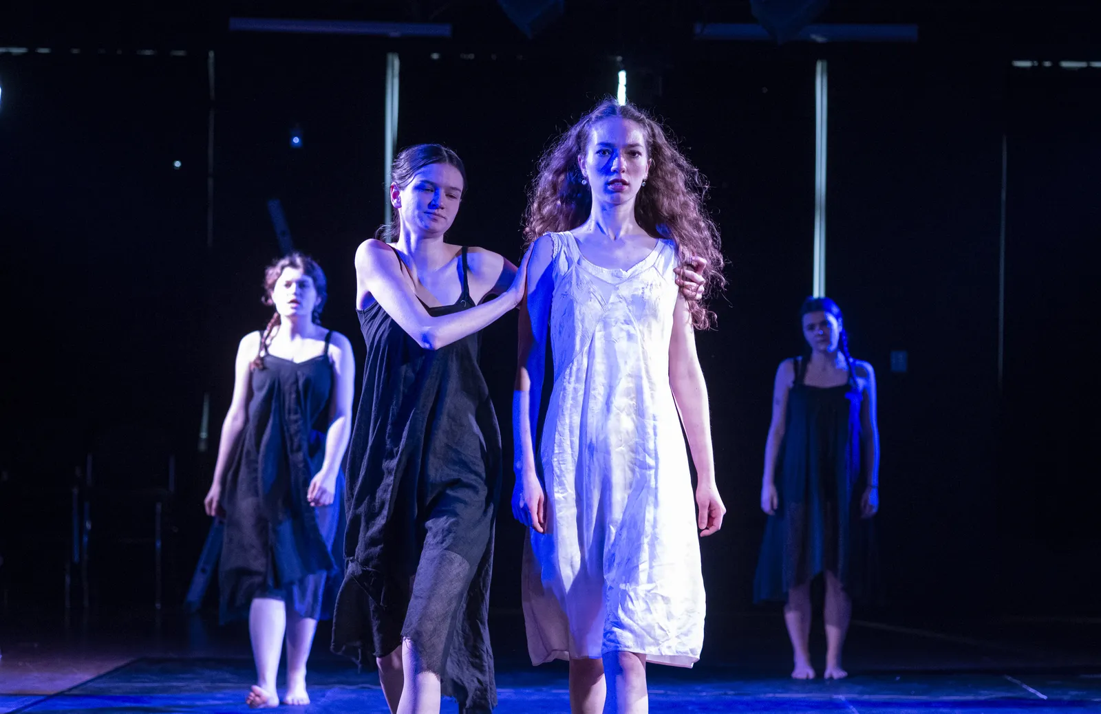 The company moving downstage together in cold blue light.