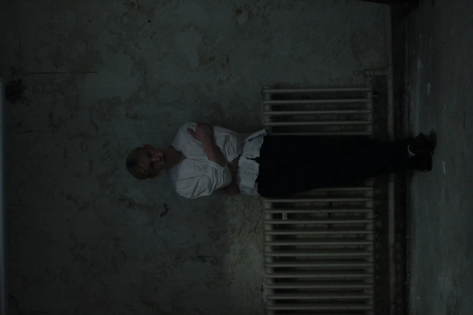 Promotional shot of a figure in white against an old radiator.