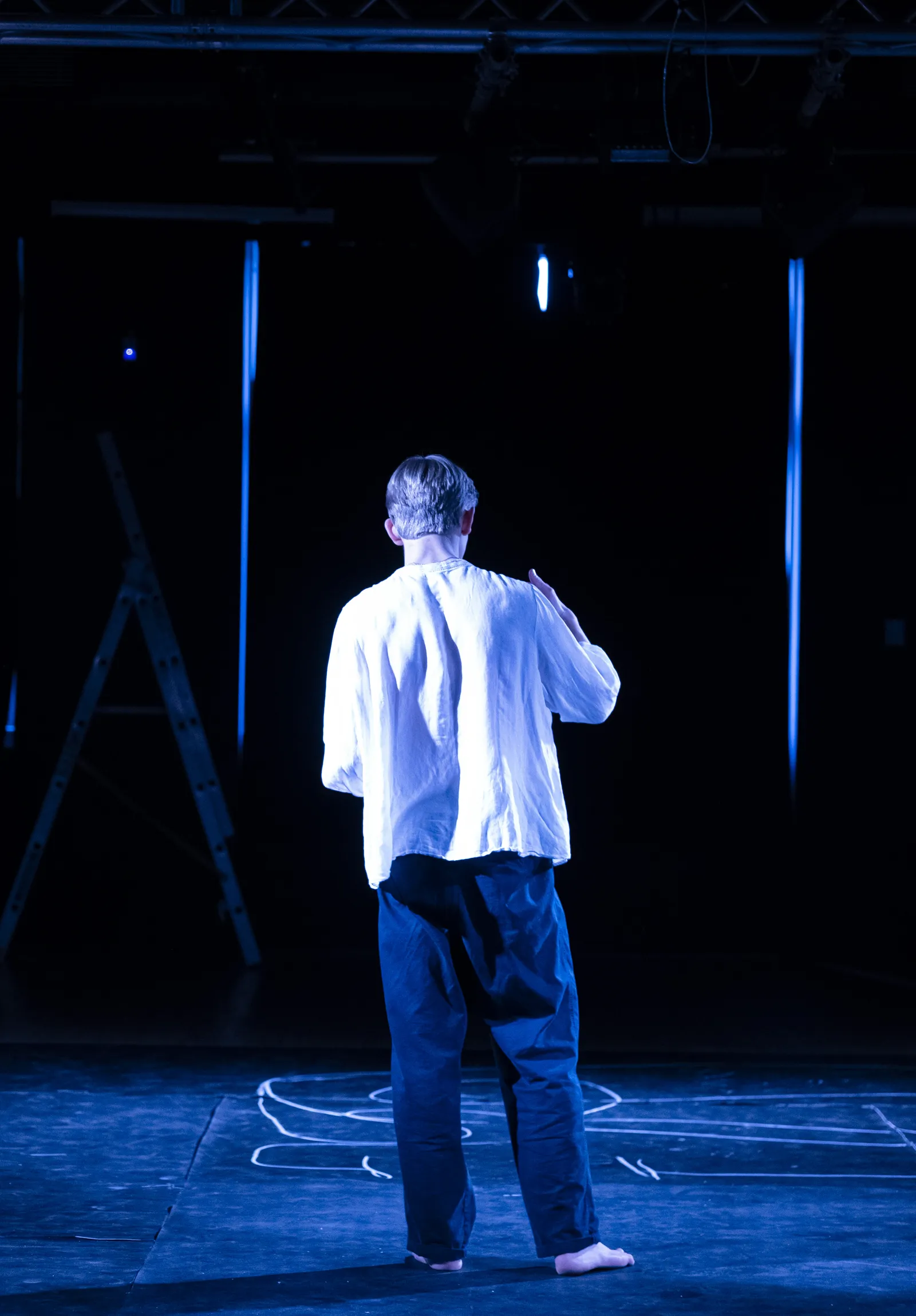 Orpheus alone with his back to the audience on the chalk-marked floor.