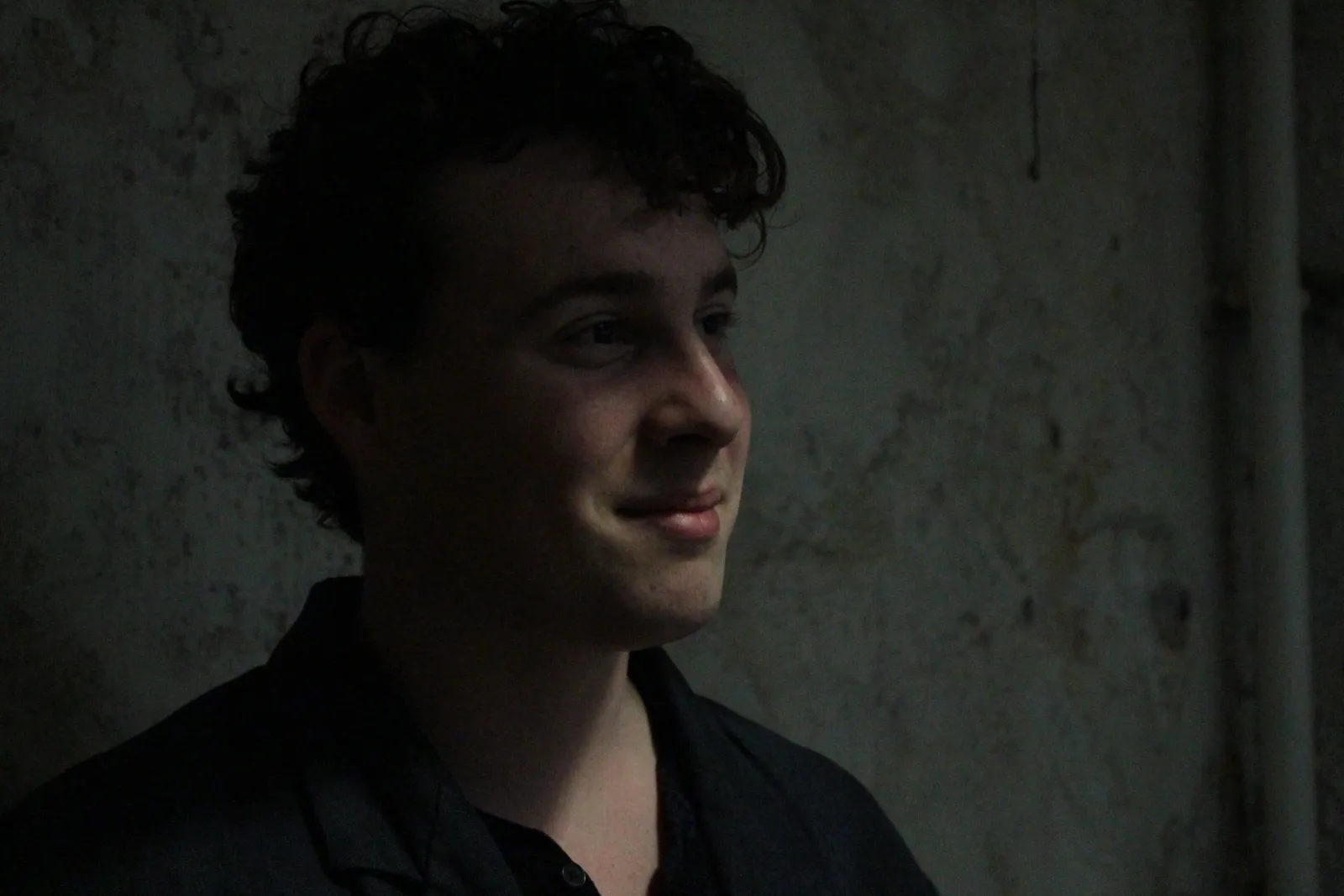 Portrait of a cast member smiling against a bare wall.