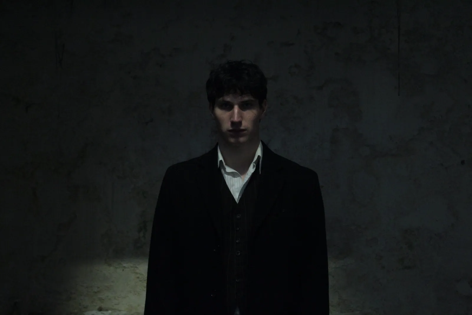 Promotional portrait of the Lord of the Underworld in a long dark coat.