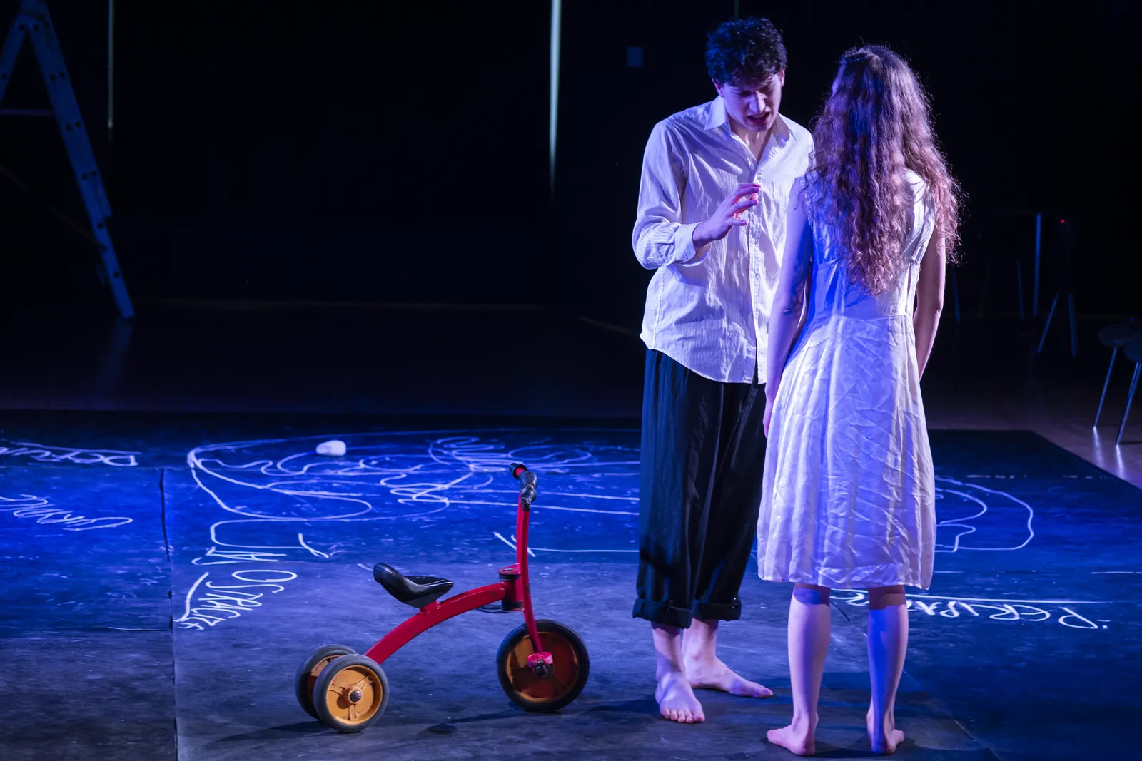 Eurydice and Orpheus standing together on the chalk-drawn stage floor.