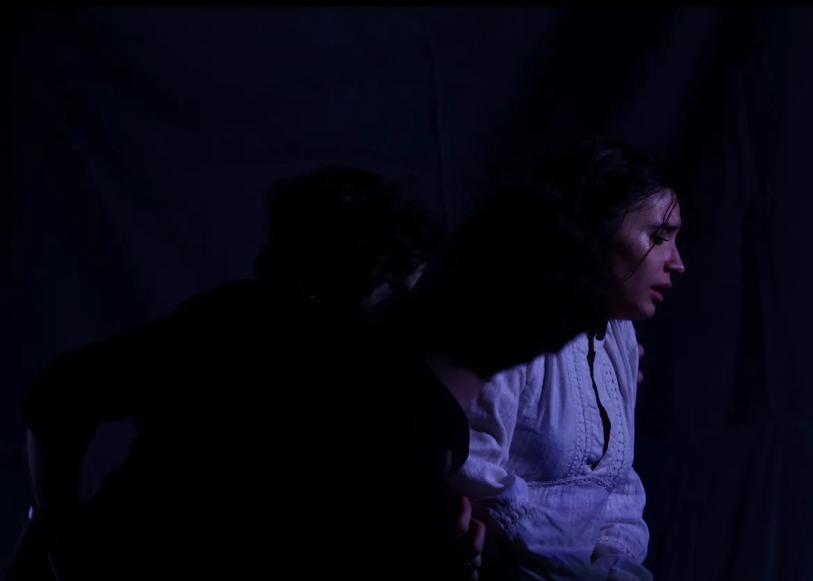 The Duchess in profile with a figure pressed close behind her in near darkness.