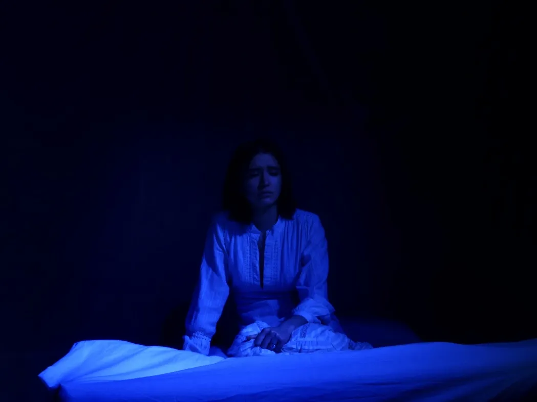 The Duchess sitting alone on the edge of her bed in dim blue light.