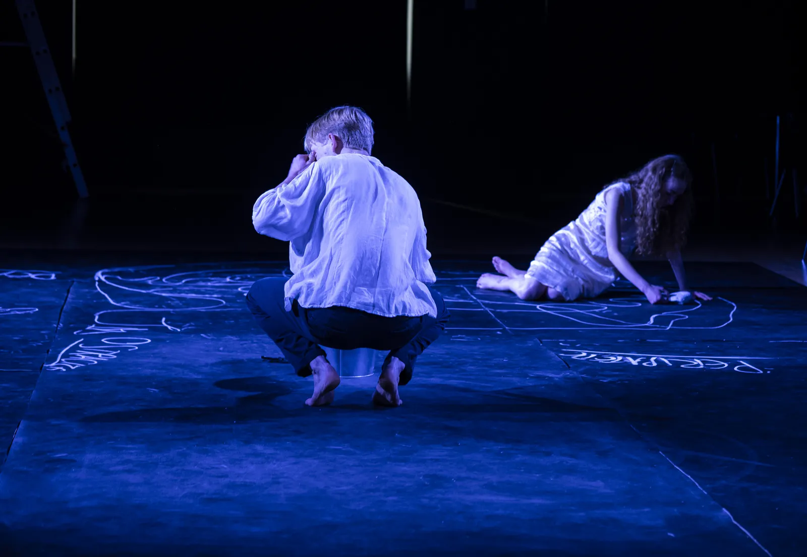 Eurydice's father crouched with his back to the audience as she lies on the floor.