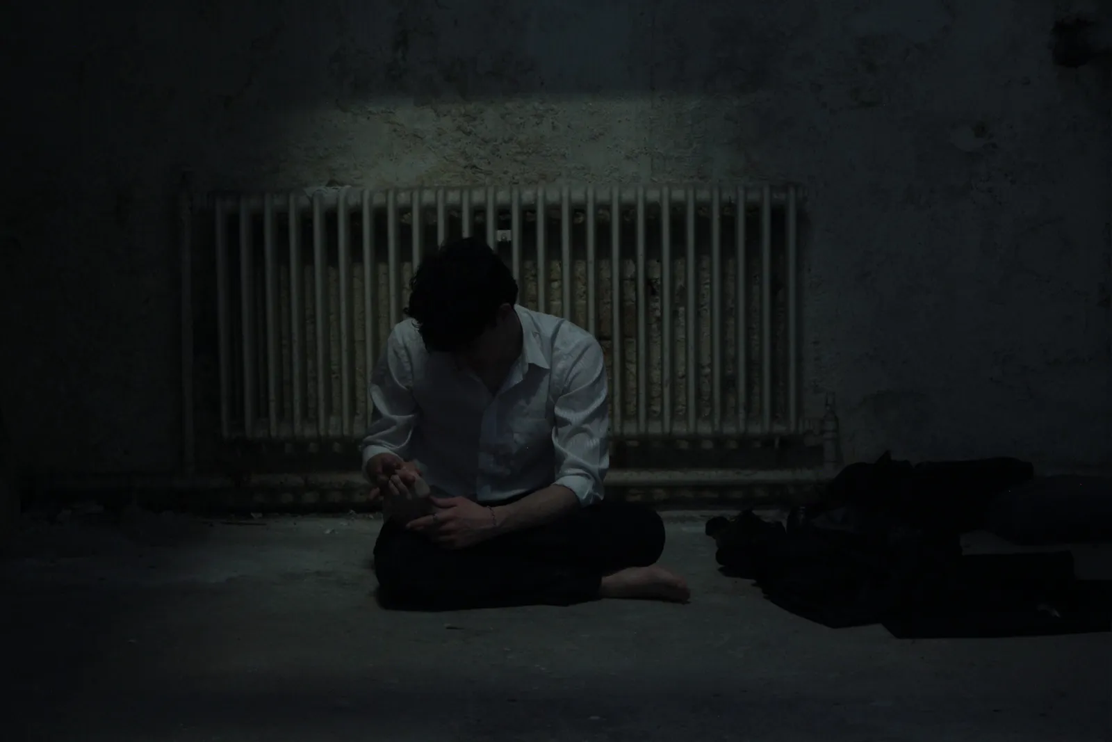 Promotional shot of a figure sitting on the floor beside a radiator.